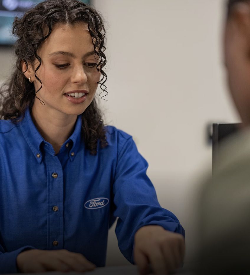 Smiling Ford service advisor in a blue Ford shirt working at the service desk