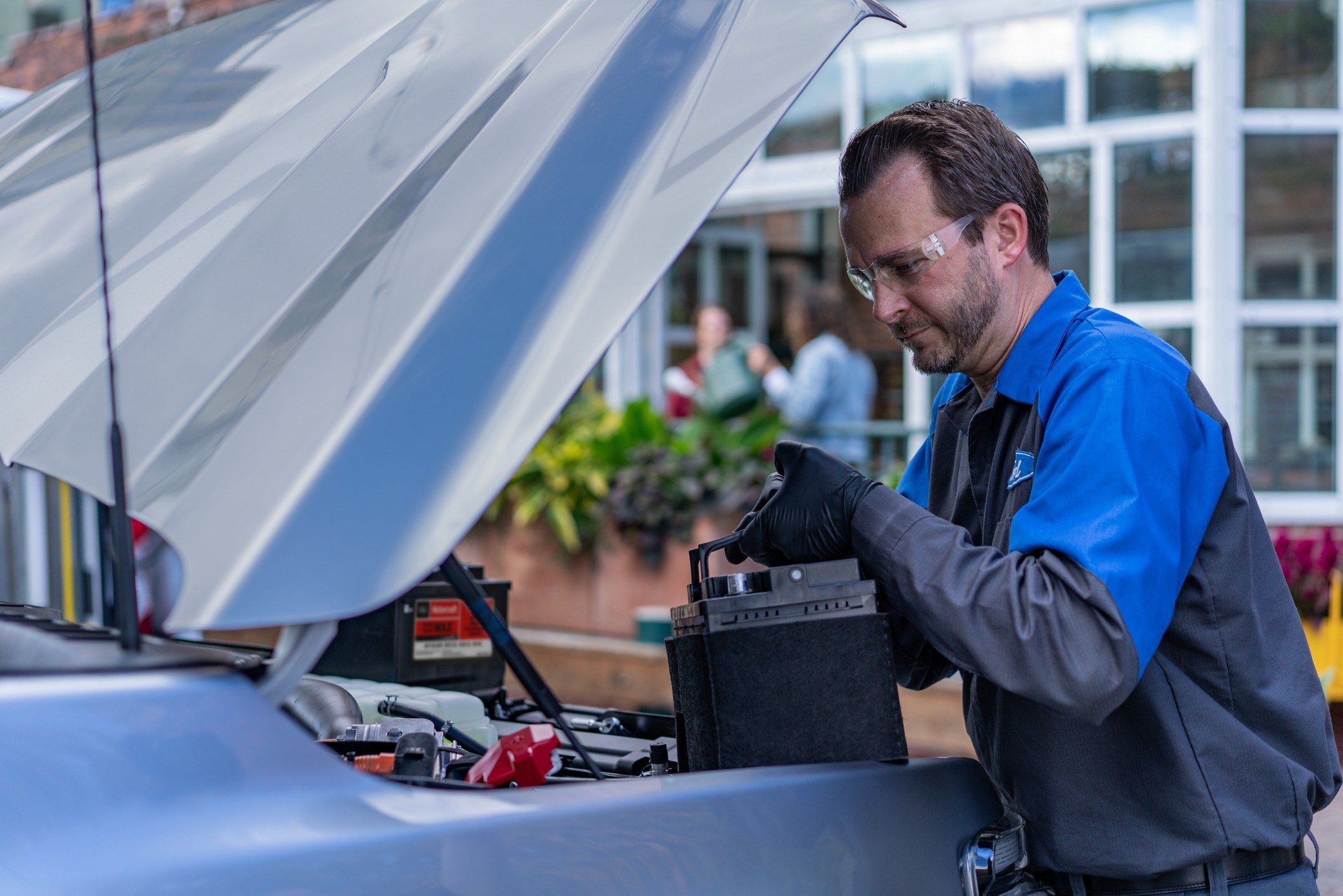 Ford technician in safety glasses testing the battery under the open hood of a vehicle