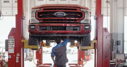 Technician working underneath a red Ford Super Duty pickup raised on a two-post lift